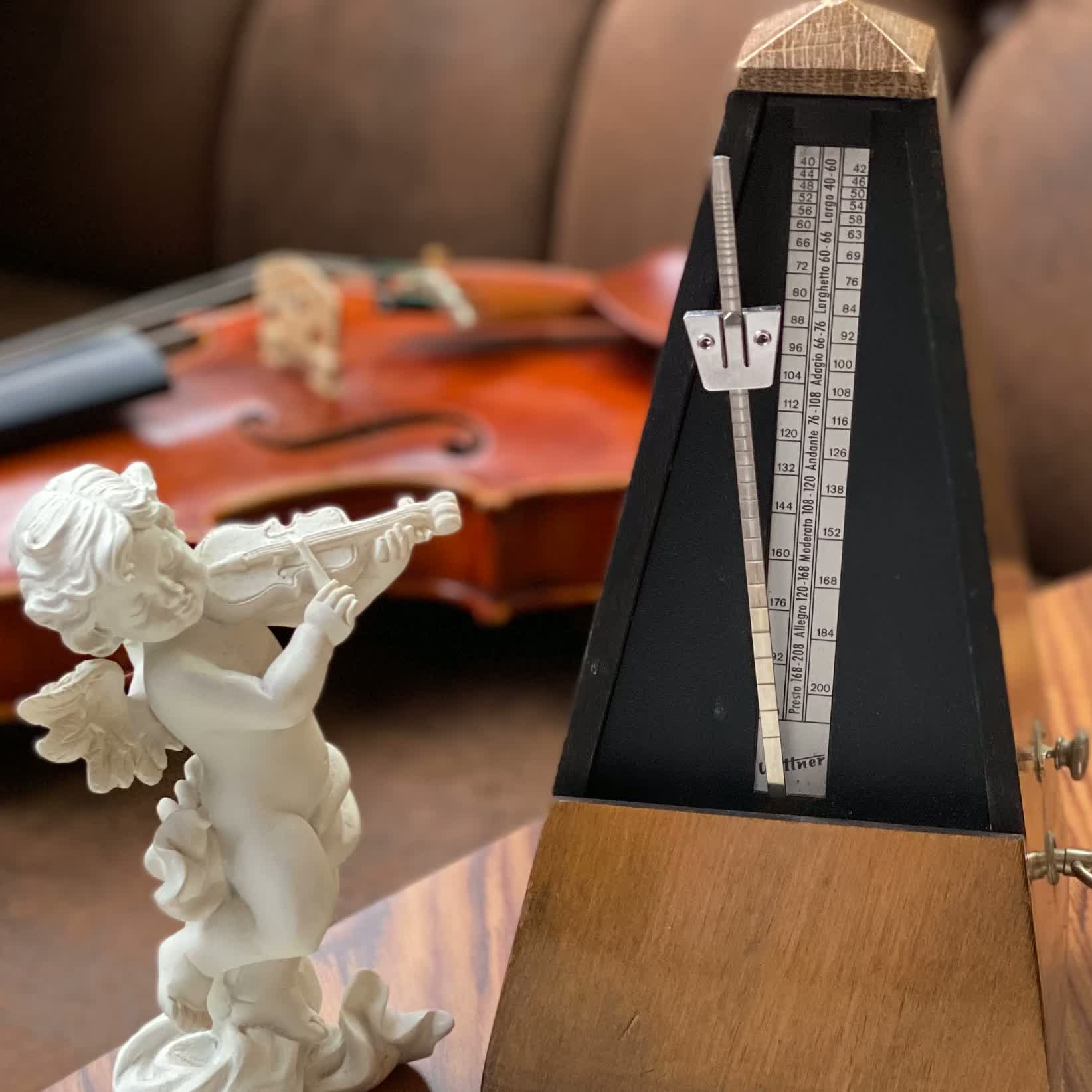 Metronom, Notenblatt und musizierende Engelsfigur neben einer Violine